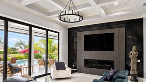 A modern living room with a fireplace, a large TV, and a view of a pool.