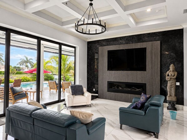A modern living room with a fireplace, a large TV, and a view of a pool.