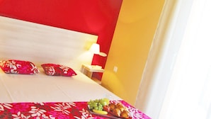 Habitación de hotel con cama, almohadas, mesita de noche y una bandeja de frutas.