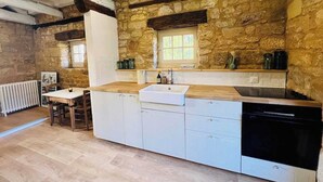 A kitchen with stone walls, a wooden countertop, a white sink, and a built-in dishwasher.