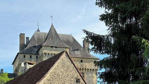A stone building with a tiled roof, arched windows, and a table with chairs outside.