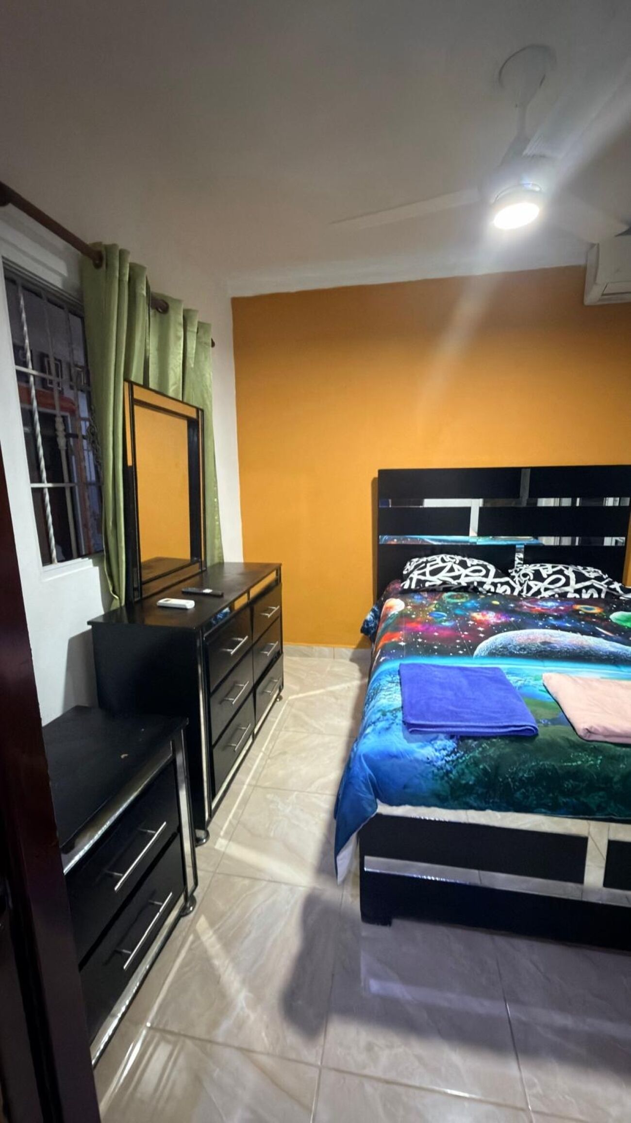Un dormitorio con cama, cómoda, espejo y ventana con cortinas.