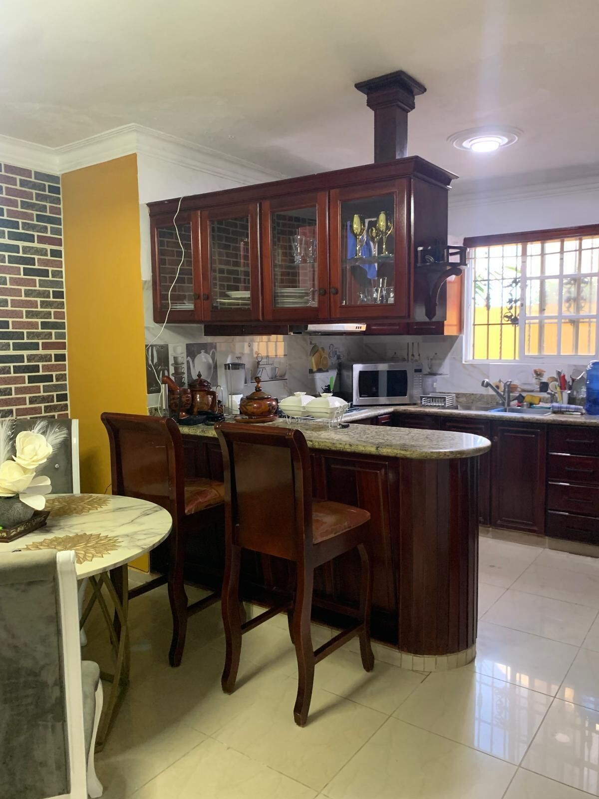 A kitchen with wooden cabinets, a marble countertop, and a dining area with chairs.