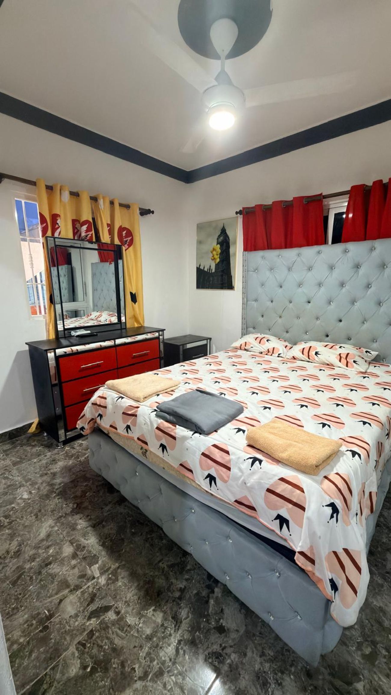 A bedroom with a bed, a dresser, a mirror, and a ceiling fan.