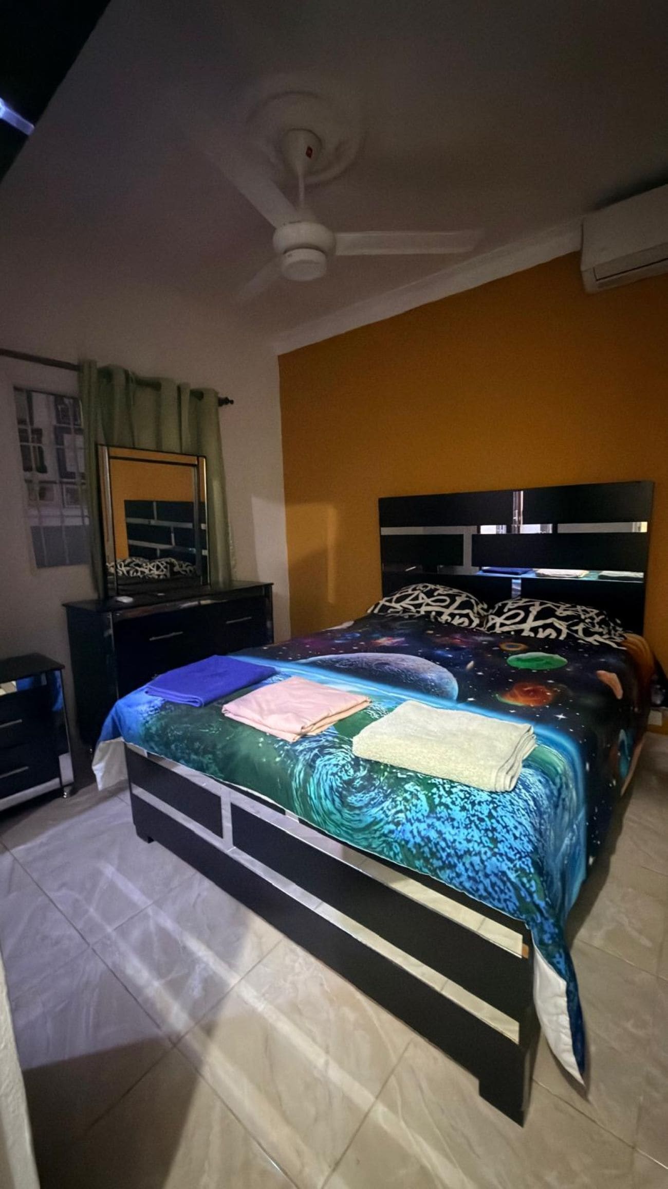 Une chambre à coucher comprenant un lit, une commode, un miroir, un ventilateur de plafond et un appareil de climatisation.