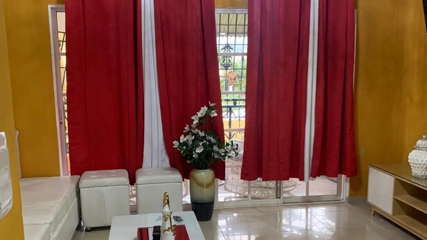 A living room with a white sofa, a coffee table with decorative items, red curtains, a chandelier, and a view through a window.