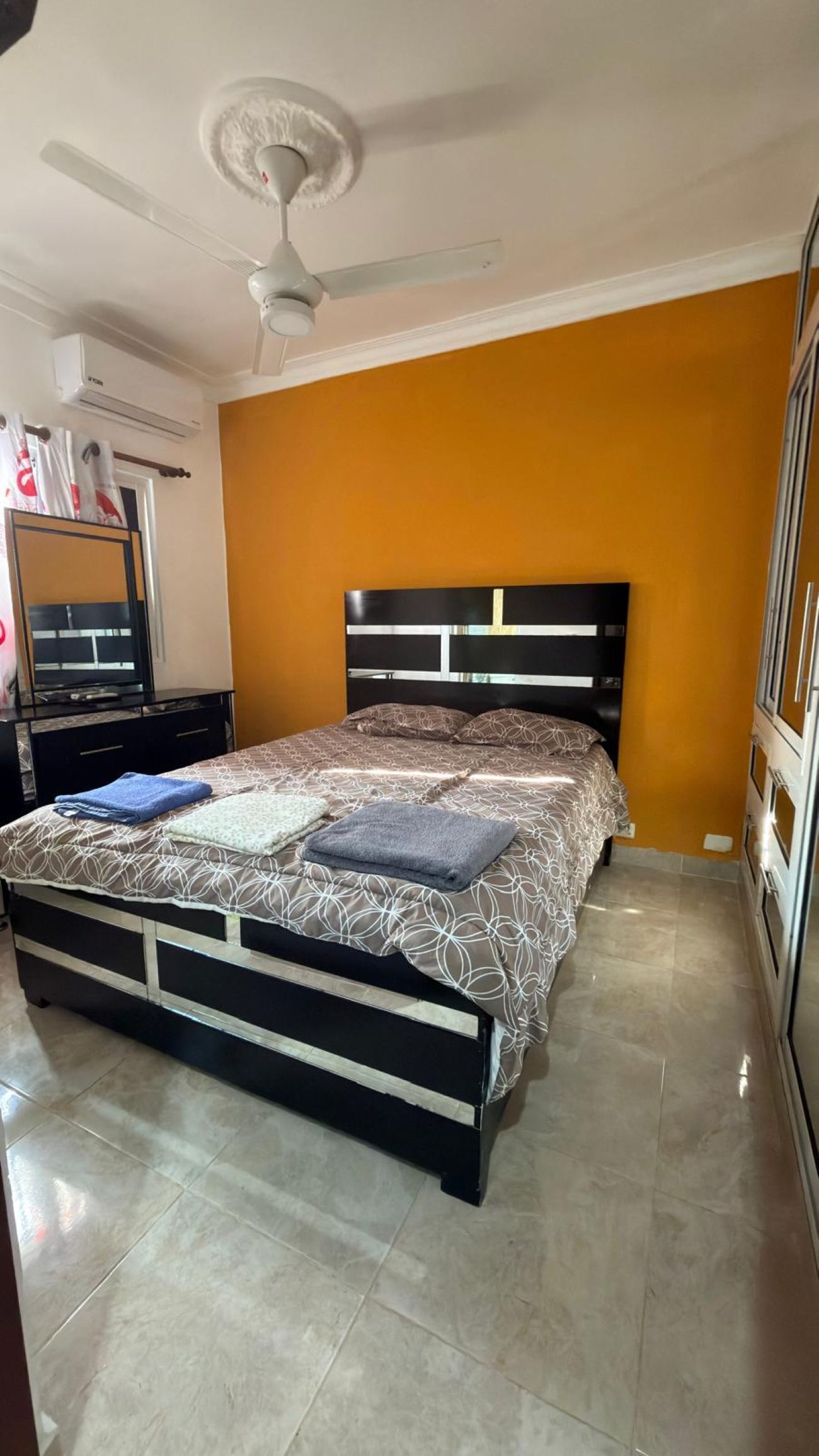 Une chambre à coucher comprenant un lit, un ventilateur de plafond, un appareil de climatisation, une commode et une armoire.