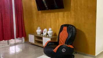 A living room with a sofa, a massage chair, a TV, and a cabinet with decorative items.