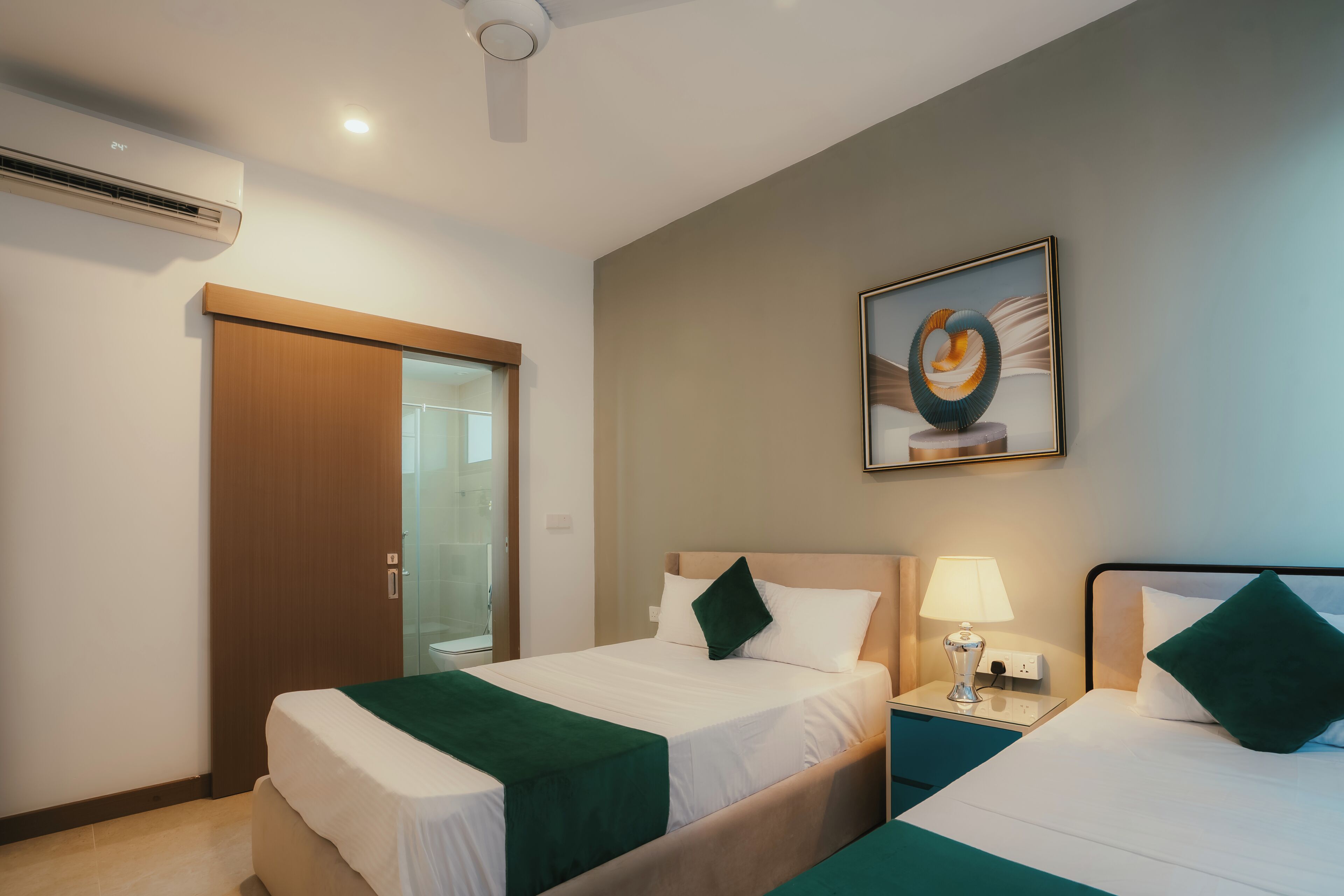 A hotel room with two beds, a glass shower enclosure, a ceiling fan, and a framed artwork on the wall.