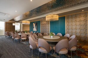 Un salón de conferencias con mesas y sillas redondas, un papel tapiz decorativo y una lámpara colgante.