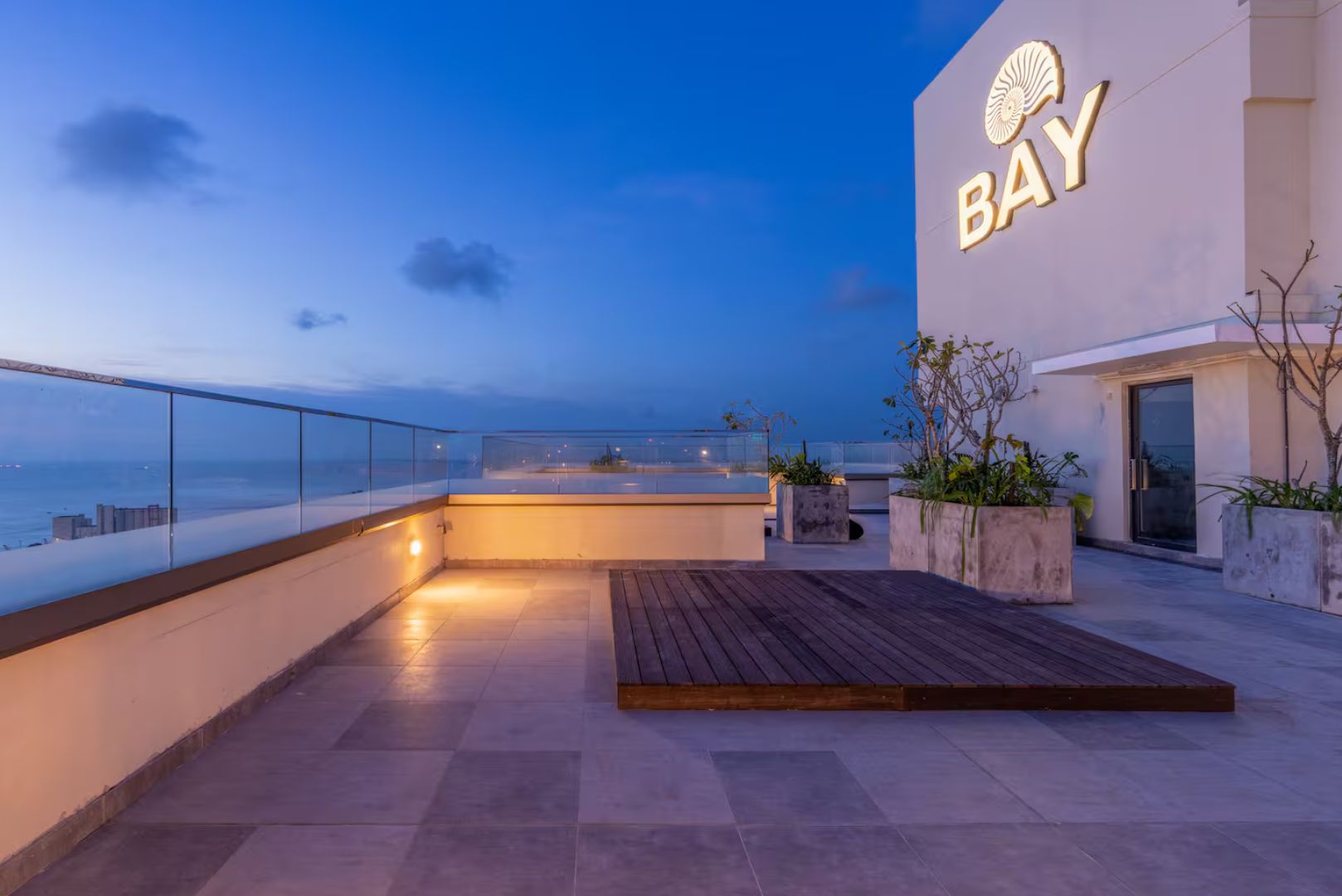 Une terrasse sur le toit offrant une vue sur la mer, un panneau indiquant « BAY » et des plantes en pot.