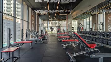 Une salle de sport équipée de divers appareils d’exercice, notamment des bancs et des haltères, et dotée de grandes fenêtres laissant entrer la lumière naturelle.