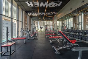 A gym with various exercise equipment, including benches and dumbbells, and large windows allowing natural light.