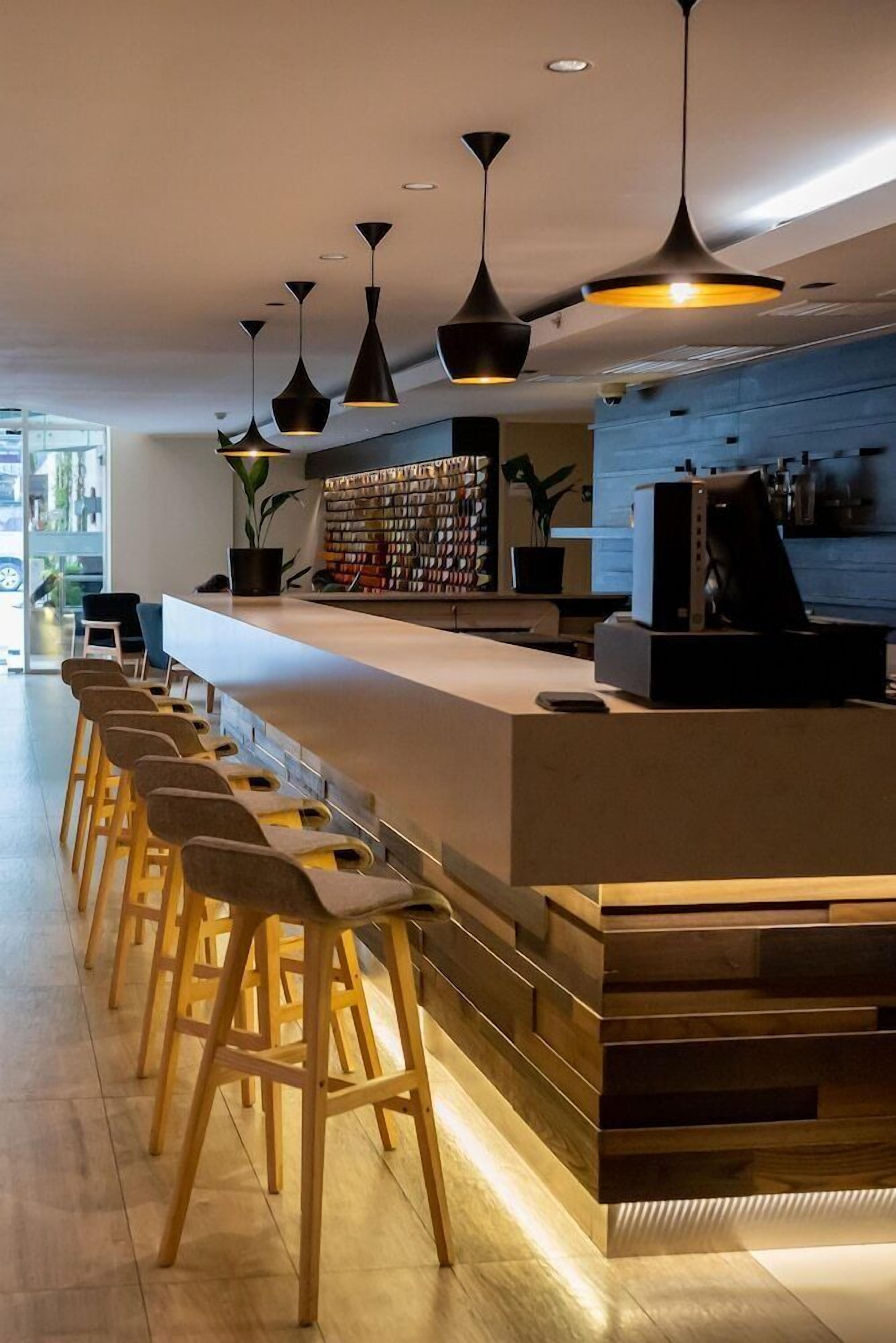 Una zona de bar moderna con una barra alargada, varios taburetes e iluminación colgante.