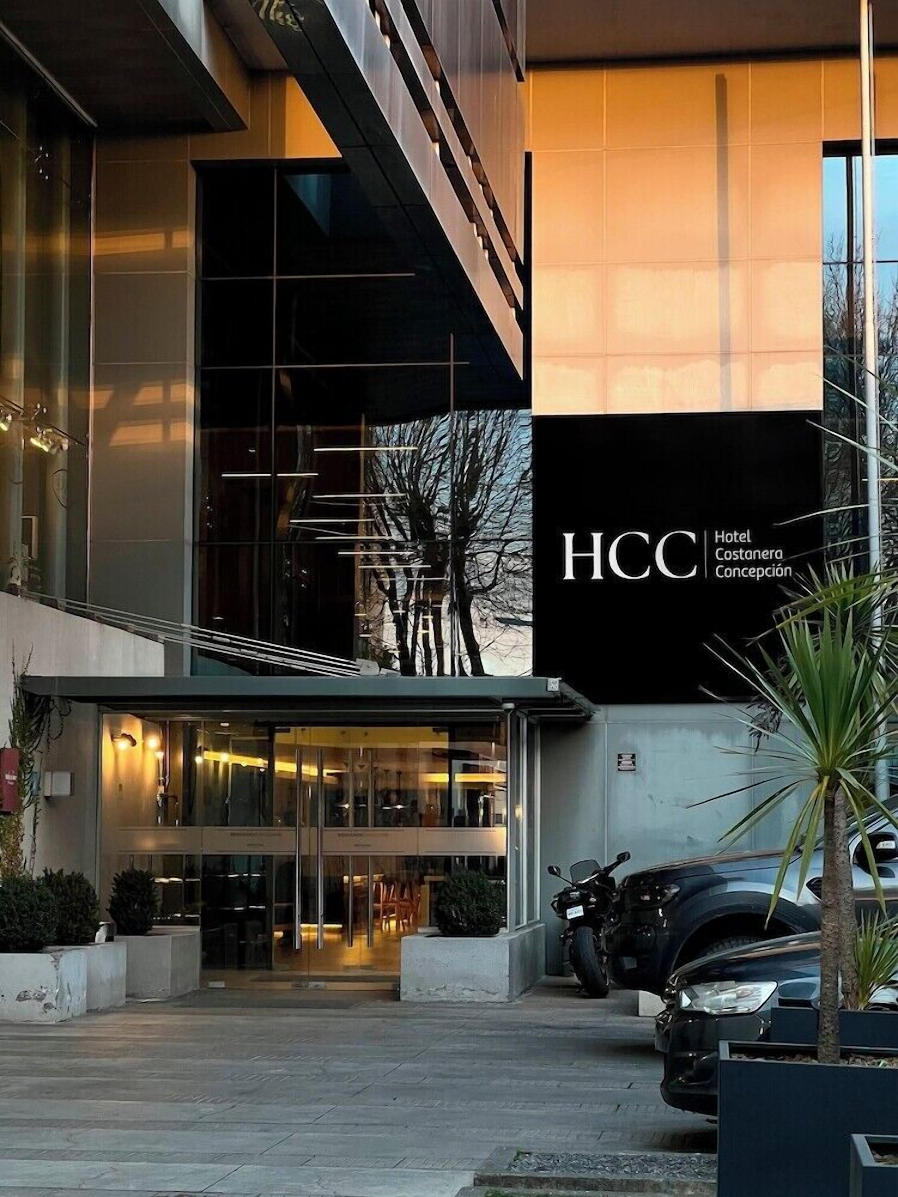 Entrada de hotel con un letrero grande, puertas de vidrio y un área de estacionamiento.