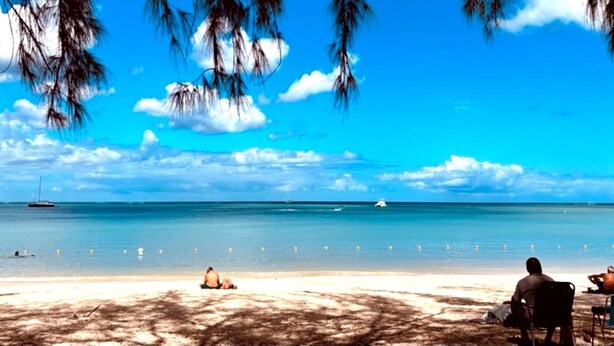Ein Strand mit badenden Menschen, Booten im Wasser und blauem Himmel.