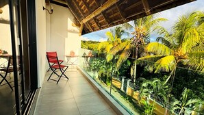 Ein Balkon mit einem roten Stuhl, einem kleinen Tisch und Blick auf Palmen.