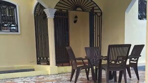 Eine überdachte Terrasse mit Fliesenboden, einem Tisch mit Stühlen und einem Zierbogen.