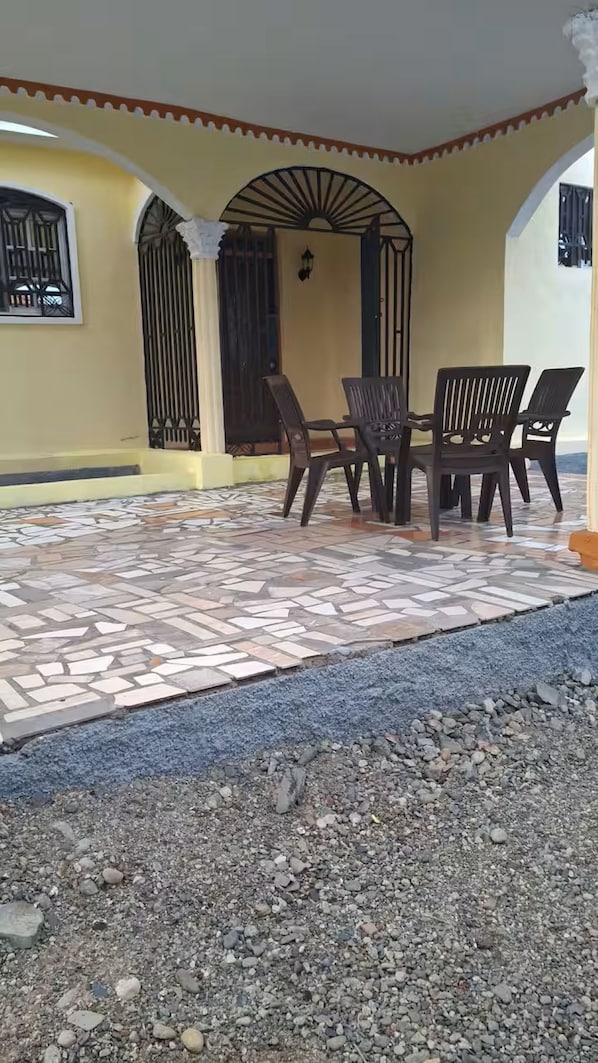 Eine überdachte Terrasse mit Fliesenboden, einem Tisch mit Stühlen und einem Zierbogen.