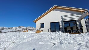 Et moderne hus med hvide facader, en træterrasse og en klar blå himmel.