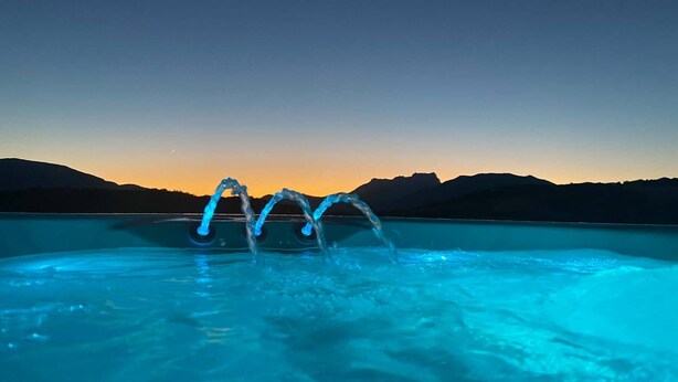 En pool med oplyste vandelementer mod en solnedgang.