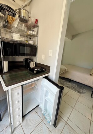 Eine kleine Küchenzeile mit Mikrowelle, Kaffeemaschine und einem Kühlschrank.