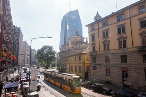 Eine Stadtbahn fährt auf einer Straße zwischen Gebäuden und parkenden Autos.