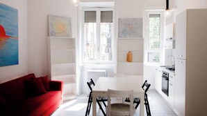 A modern kitchen with white cabinetry, a dining table with chairs, a red sofa, and artwork on the walls. - 5 minutes from milan central station- 3 minutes from piazza repubblica- comfort (Milano)