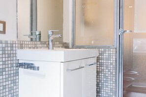 Ein Badezimmer mit weißem Waschbecken, chromfarbenem Wasserhahn und gefliesten Wänden.