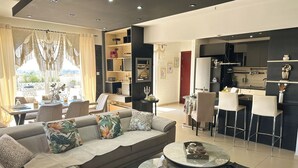 A modern living room with a sofa, coffee table, and dining area. - Modern Penthouse Overlooking Pool (Pyla)