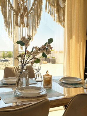 A dining table with a vase of flowers, a glass candle holder, and a decorative jar. - Modern Penthouse Overlooking Pool (Pyla)