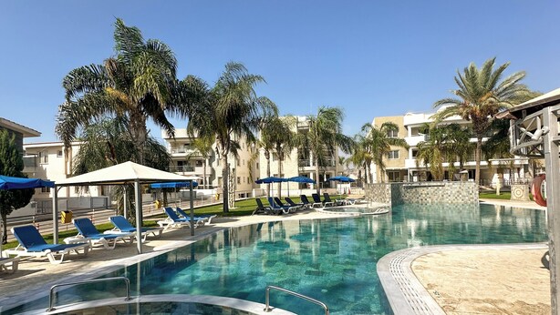 A swimming pool with lounge chairs and palm trees, surrounded by buildings. - Modern Penthouse Overlooking Pool (Pyla)