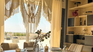A dining area with a table set for two, chairs, a vase with flowers, and a view through the window. - Modern Penthouse Overlooking Pool (Pyla)