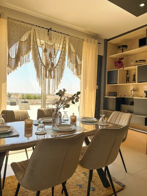 A dining area with a table set for two, chairs, a vase with flowers, and a view through the window. - Modern Penthouse Overlooking Pool (Pyla)