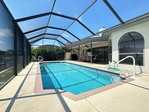 Ein Schwimmbad mit Glasumrandung, eine Terrasse mit Stühlen und ein überdachter Außenbereich mit Sitzgelegenheiten.