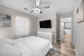 A bedroom with a bed, a ceiling fan, a TV, and a walk-in closet.