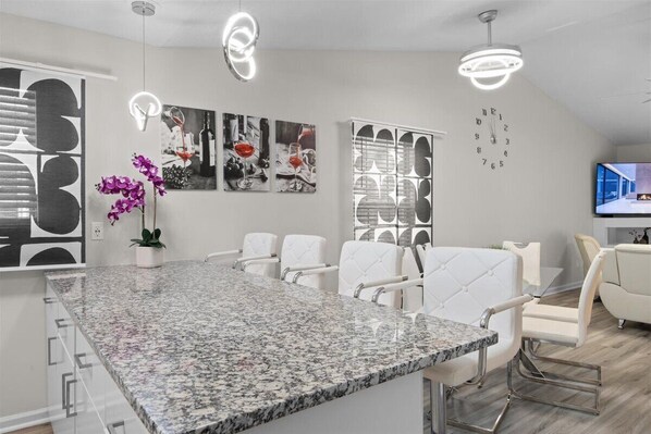 A modern kitchen with a granite countertop, white chairs, and pendant lighting.