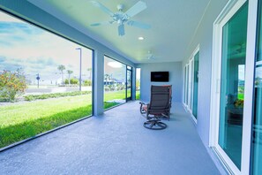 Ein überdachter Außenbereich mit Deckenventilator, einem Sessel und einem an der Wand befestigten Fernseher.