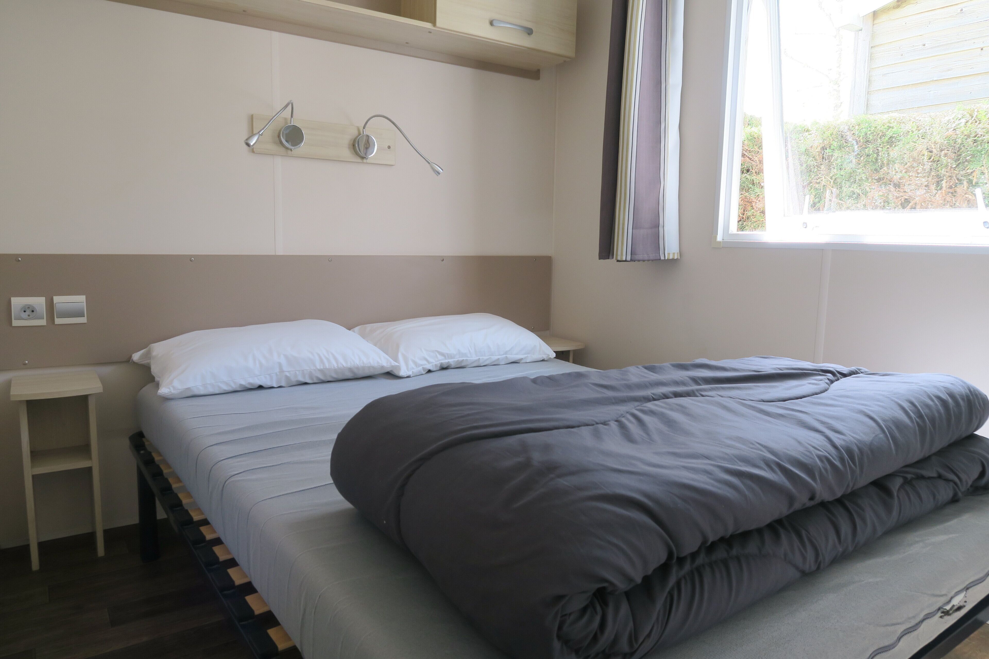 Une chambre à coucher comprenant un lit, des tables de chevet, une fenêtre et un luminaire fixé au mur.