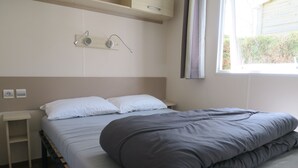 Un dormitorio con cama, mesitas de noche, ventana y una lámpara fijada a la pared.