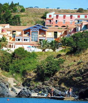 A coastal hotel with multiple buildings, a rocky shoreline, and people by the water. - Hillside Mediterranean Stay for 6 (Cerbère)