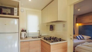 Una kitchenette compacta con refrigerador, estufa y pileta, junto a una cama con cabecera y almohada.