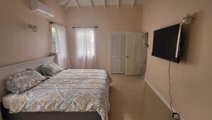 Ein Schlafzimmer mit einem Bett, einem Fernseher, einem Fenster mit Vorhängen und einer Tür.