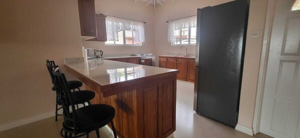 Eine Küche mit Kochinsel, Holzschränken, einem schwarzen Kühlschrank und einem Fenster mit Vorhang.