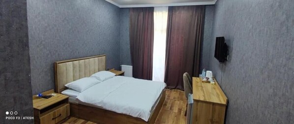 Une chambre d’hôtel comprenant un lit, des tables de chevet, un bureau, une chaise, une télévision et une fenêtre avec des rideaux.