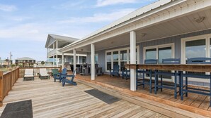 A covered outdoor deck with wooden flooring, multiple seating areas, and a view of the surrounding area. - Catch & Release ~ Bay Front ~ Sleeps 12 (Dauphin Island)