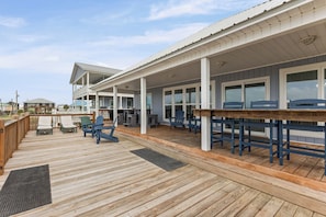A covered outdoor deck with wooden flooring, multiple seating areas, and a view of the surrounding area. - Catch & Release ~ Bay Front ~ Sleeps 12 (Dauphin Island)