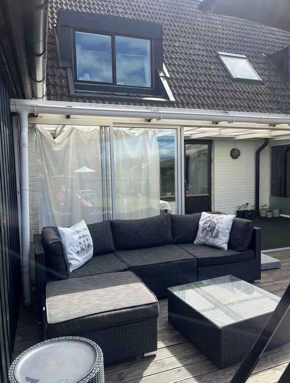 A covered outdoor seating area with a sofa and ottoman, a window, and a door.