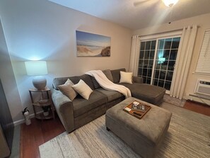 A living room with a grey sofa, a white rug, a side table with a lamp, and a painting on the wall.