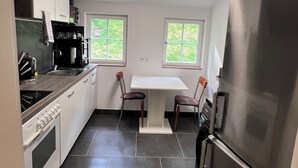 Et moderne køkken med indbygget ovn, køleskab og spiseplads med to stole og et bord.